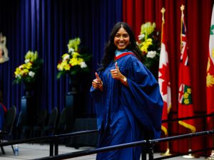 A Brock University graduate wearing a blue gown gives the thumbs up sign on the stage during her convocation.