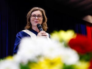 Brock University President Lesley Rigg holds a microphone and smiles on stage.