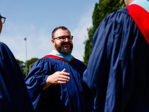 A Brock University graduate stands outside with two fellow graduates with a blue sky in the background.