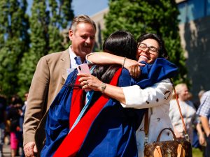 A loved one hugs a person in a blue academic robe outside after a university graduation ceremony.