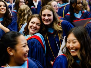 A group of graduates in graduation gowns smile at one another while gathered together.