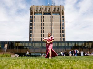 A woman in a formal dress holds flowers while standing outdoors in front of Brock's Schmon Tower.