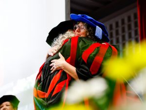 Two people in Convocation gowns hug.