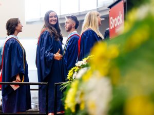 A group of people in graduation gowns wait to cross the Convocation stage.