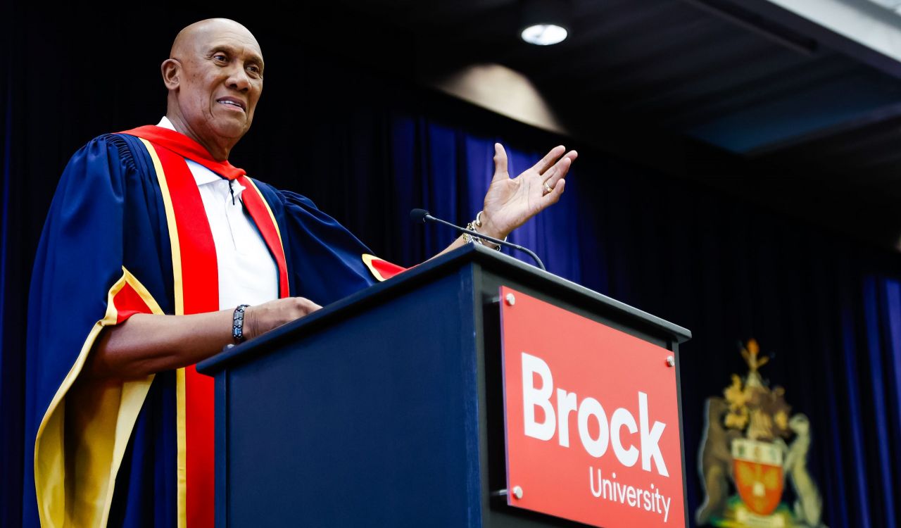 A man stands at a podium with his hand raised speaking to an unseen crowd.