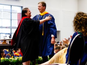 A man and woman wearing ceremonial gowns hug on stage at Brock University’s 115th Convocation ceremony.