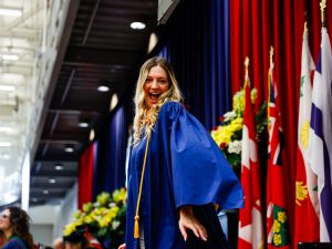 A woman wearing a blue convocation gown smiles on stage at Brock University’s 115th Convocation ceremony.