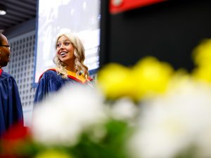 A woman surrounded by flowers smiles before crossing the stage at Brock University’s 115th Convocation ceremony.