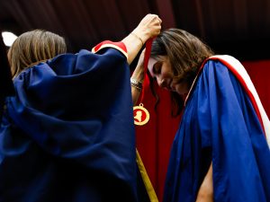 A woman wearing a blue ceremonial gown bows her head to receive a medal with a ribbon from another woman on stage at Brock’s 115th Convocation ceremony.