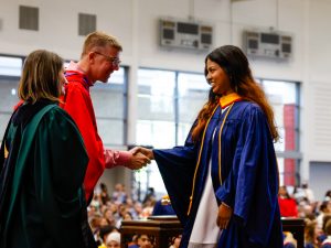 A woman shakes a man’s hand on stage during a graduation ceremony at Brock University. Both are wearing academic robes.