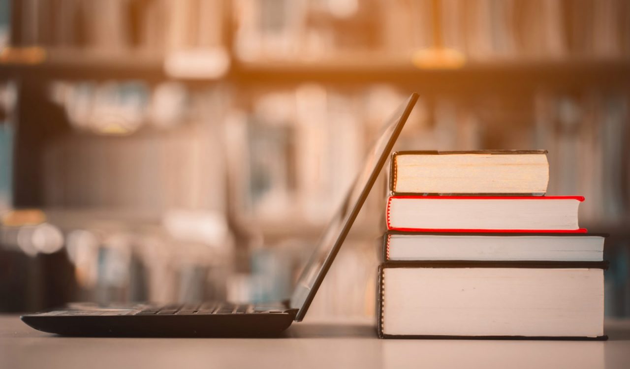 Laptop on a table leaning next to a pile of books.