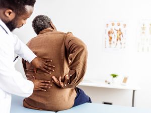 A doctor examines the lower back of a patient who is sitting on a bed in a doctor's office.