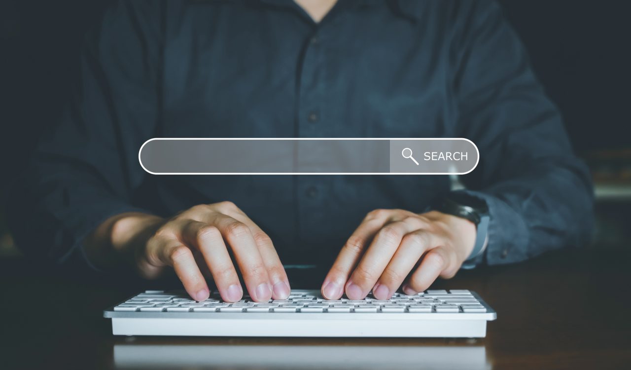 Close-up of hands typing on a keyboard with a search bar floating above them.