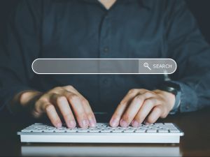 Close-up of hands typing on a keyboard with a search bar floating above them.