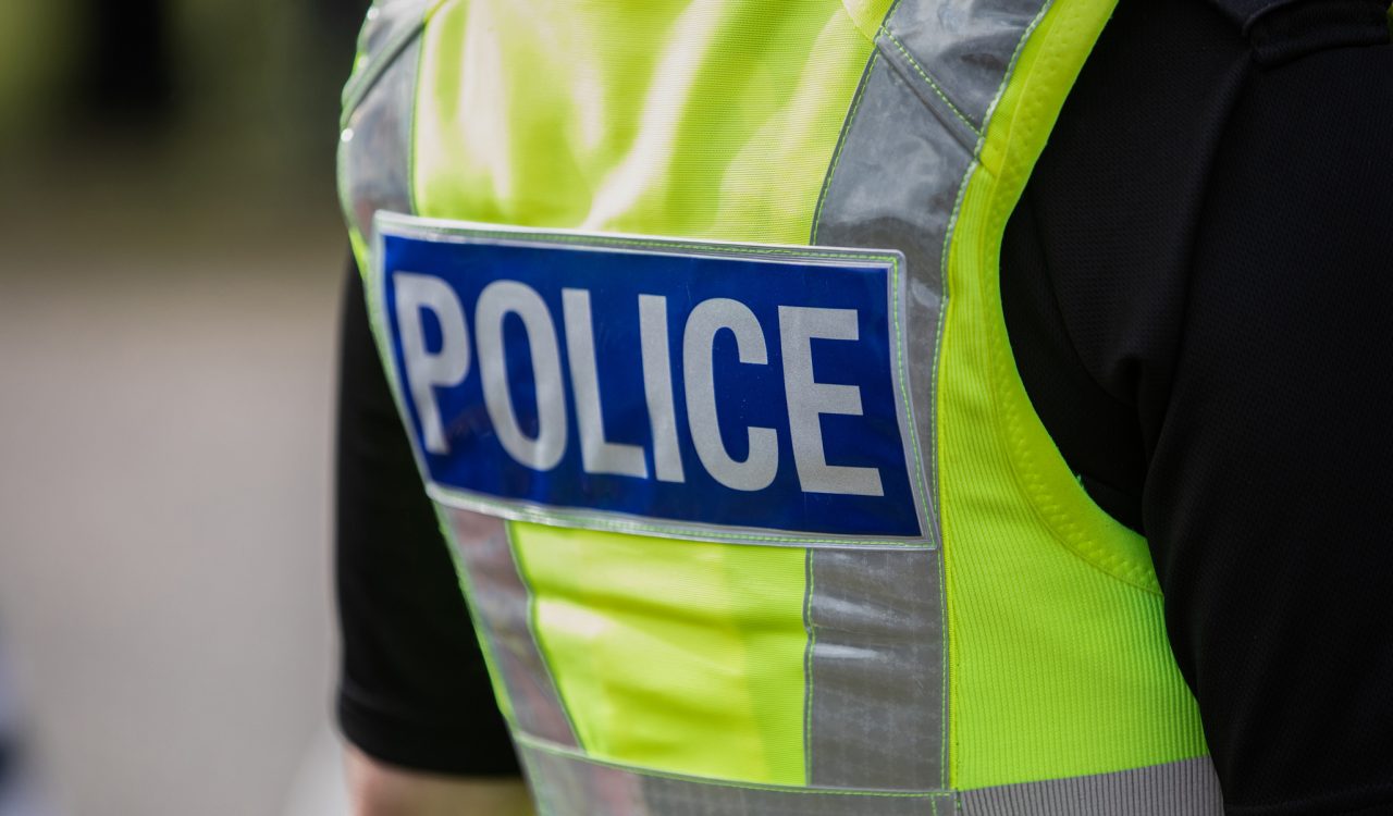 Close-up view of a police officer's back. They are wearing a yellow safety vest with the word "police" on it.