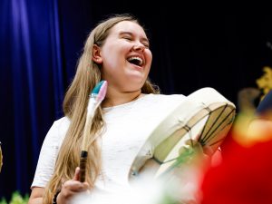 A woman plays an Indigenous drum during a university graduation ceremony.