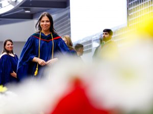 A woman in a blue academic robe smiles while crossing the stage during a university graduation ceremony.