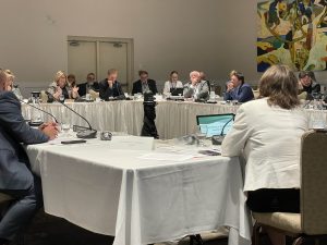 A large group of people sit at tables during a meeting.