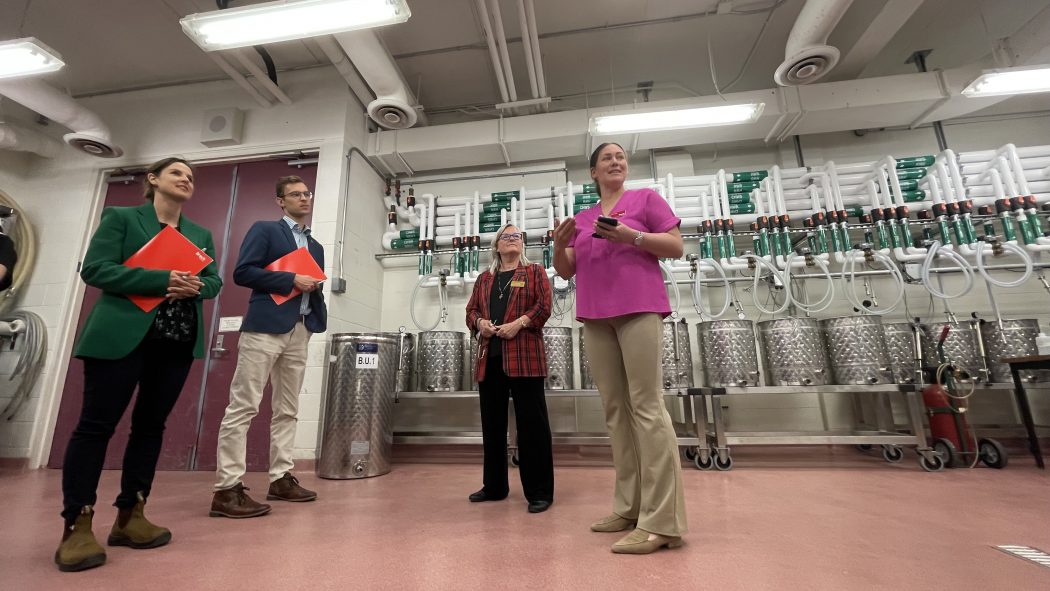 Four people standing in front of a wall of equipment in a lab.