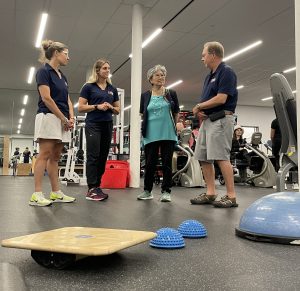 Four people standing by exercise equipment.