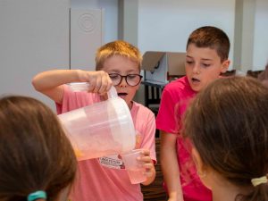 Two elementary school children pour pink lemonade from a pitcher.