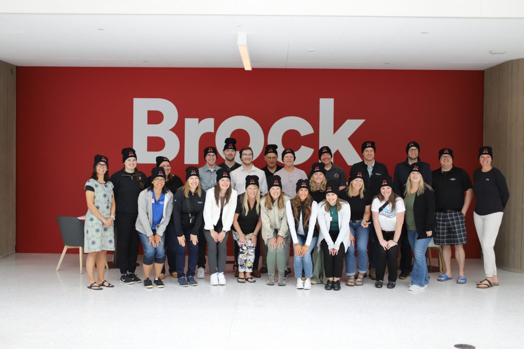 A large group of people pose for a photo in front of a red wall with the word Brock written on it in white.