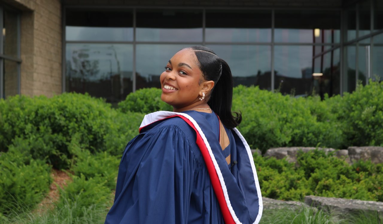 A person wearing wearing a blue academic robe smiles over her shoulder for the camera.