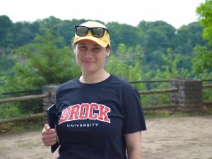 Jennifer Holzer, wearing a Brock University T-shirt and yellow baseball cap with sunglasses balanced on the brim, holds a tablet for survey data collection at the Niagara Glen.