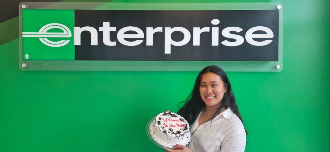 Jerica Galo holds a cake in front of an Enterprise Canada sign. 