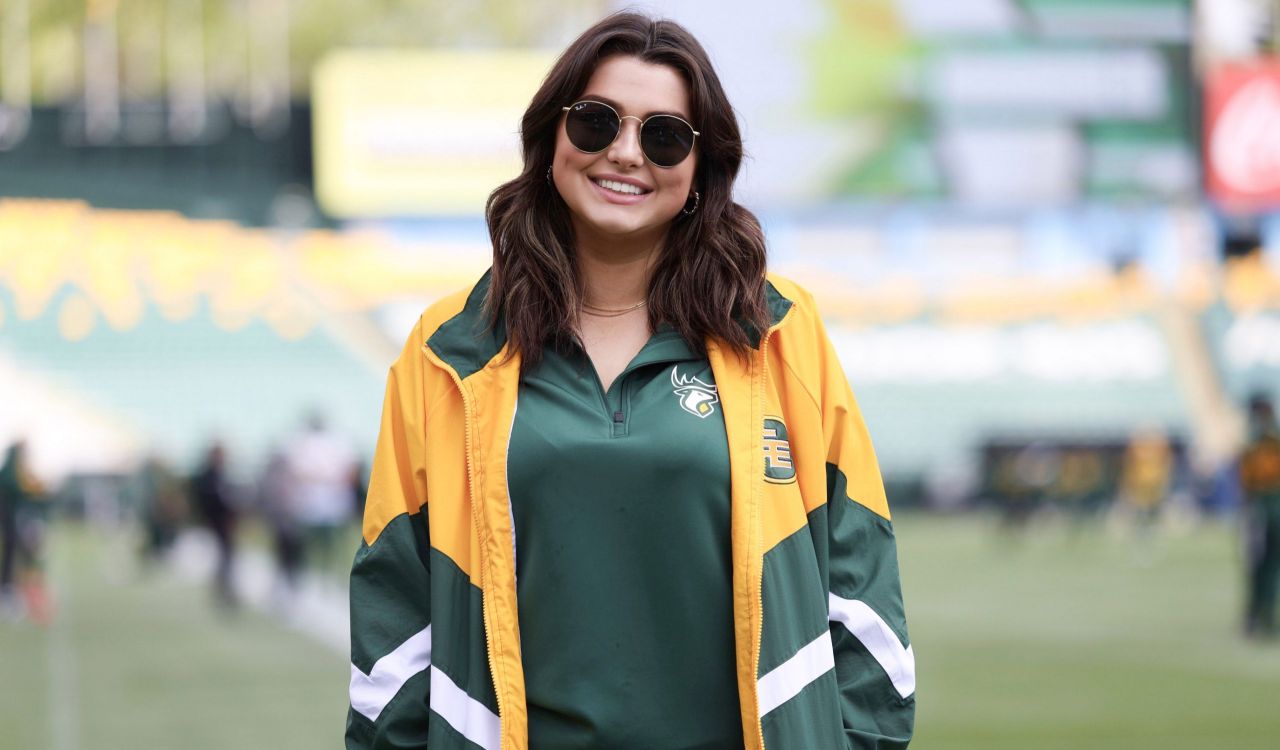 Brock University Sport Management student Kae Allison stands on the Edmonton Elks football field. She is wearing sunglasses and a team windbreaker jacket and shirt.