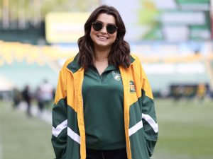 Brock University Sport Management student Kae Allison stands on the Edmonton Elks football field. She is wearing sunglasses and a team windbreaker jacket and shirt.