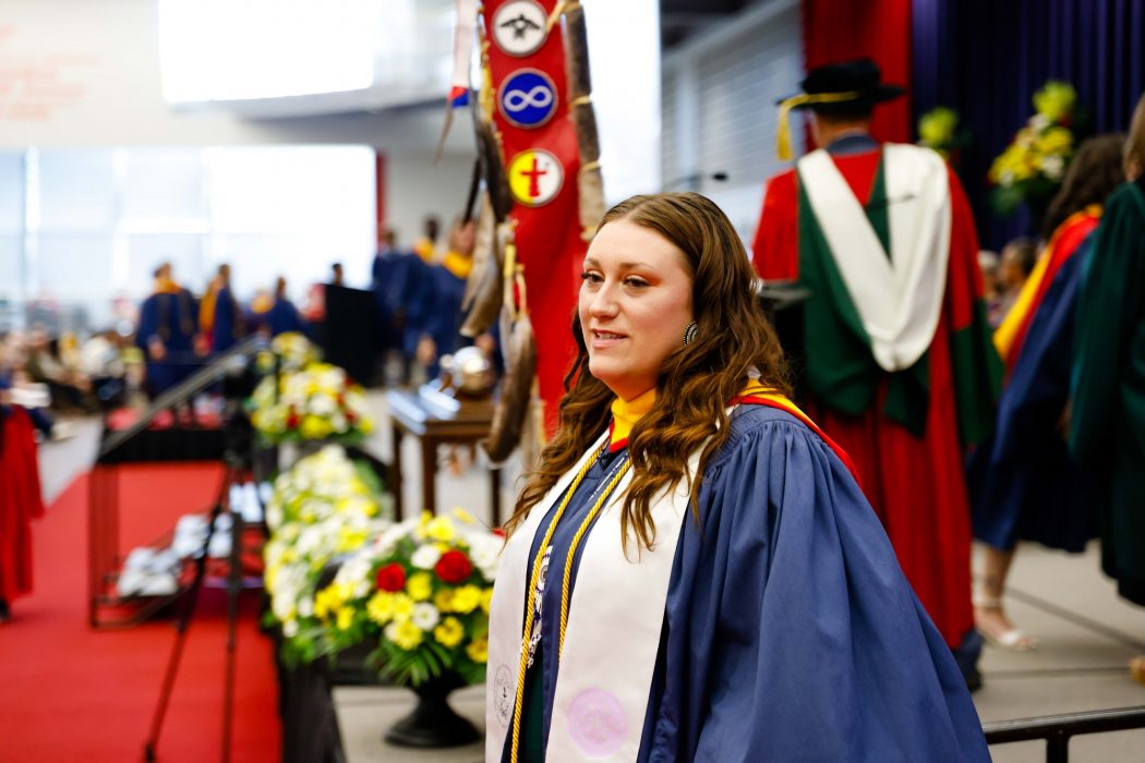 A photo of Kaitlyn Austin wearing a convocation gown leaving the stage after receiving her diploma.