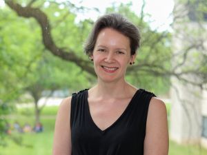 Waist-up view of Associate Professor of Psychology Karen Campbell standing in front of a window, with out-of-focus leaves and branches in the background.