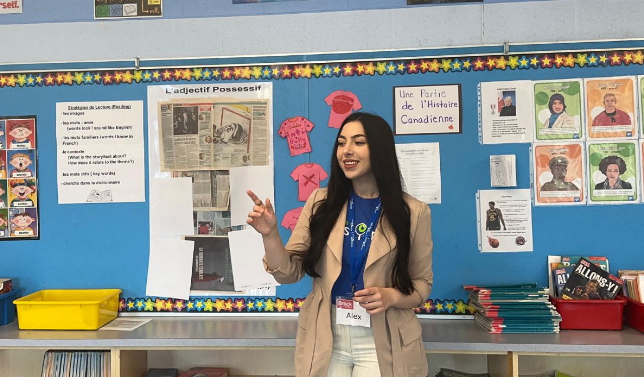 Brock University Biological Sciences student Alexandra Leone engages children in an interactive science-based activity. She is speaking at the front of an elementary school classroom.