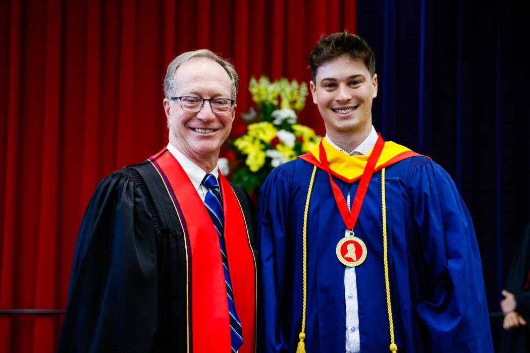 Two men stand on stage with a medal during Brock University’s convocation.