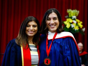 A young woman wearing a blue academic robe and a medal poses for a photo next to a woman in academic regalia.