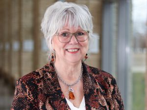 A woman wearing glasses and a colourful blazer stands at Brock University.