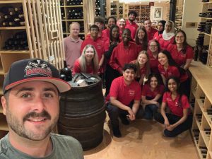 People in red shirts pose for a group selfie behind a man taking the photo.