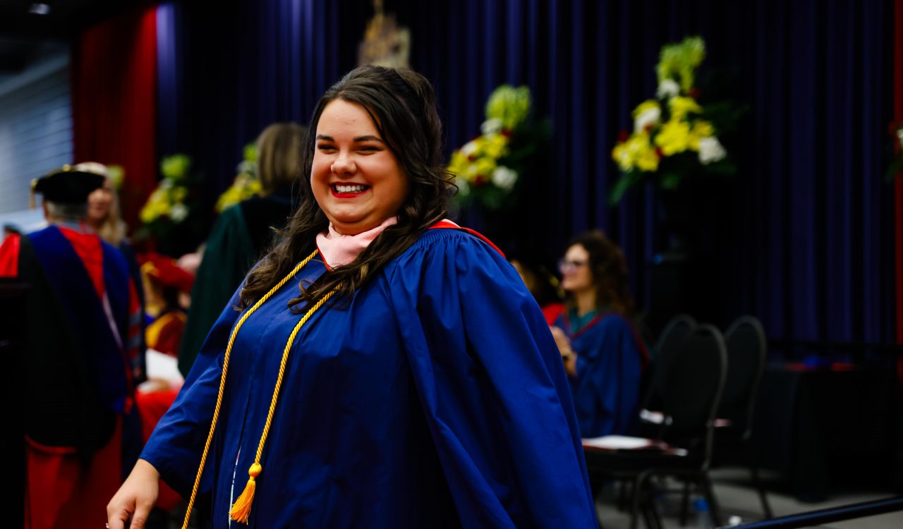 Samantha Bowman smiles while wearing a blue graduation gown on the stage at Brock University's 115th Convocation ceremonies.