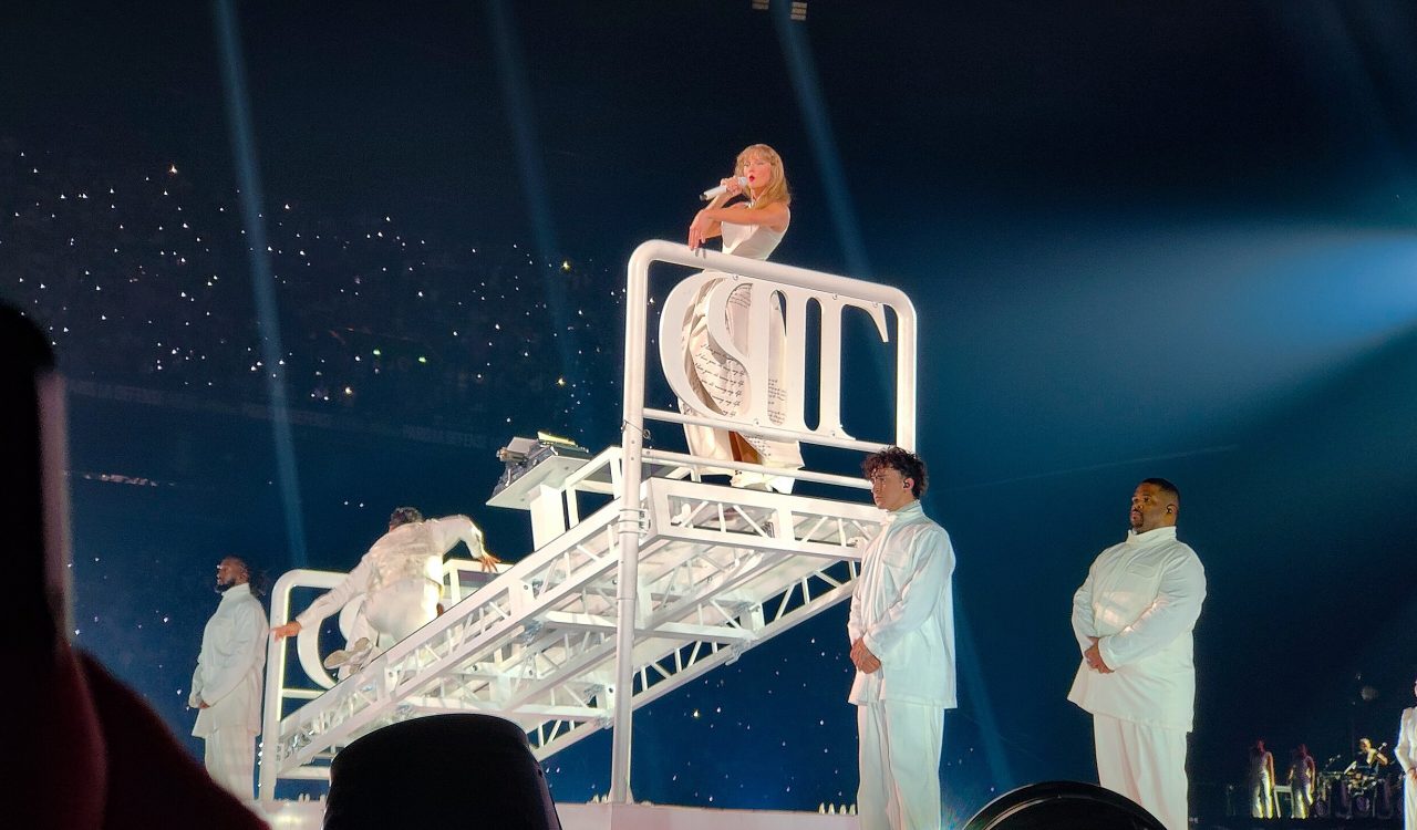 A woman sings on stage in a white dress while standing on a white platform.