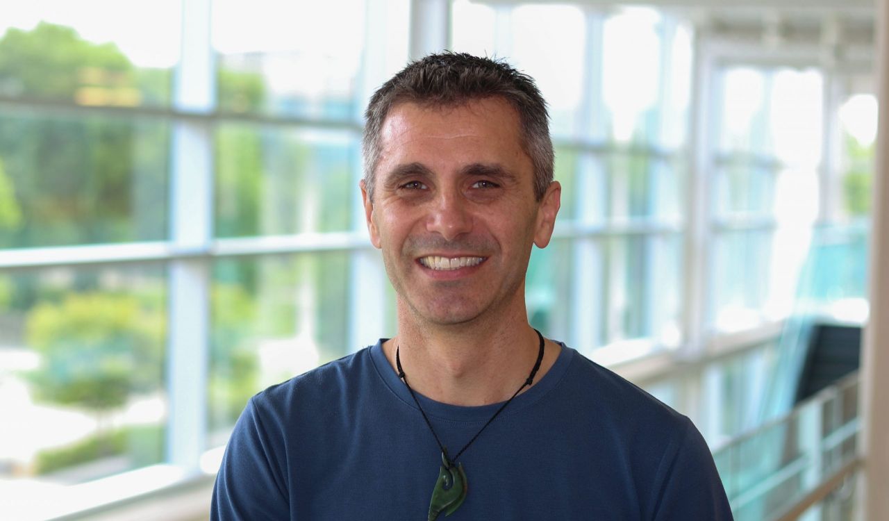 Head and shoulders photo of Professor of Kinesiology Toby Mündel with a sunny hallway and windows in the background.