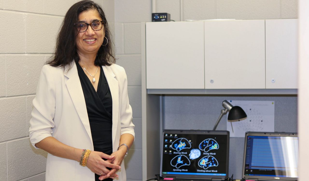 A woman standing next to two computer screens with images of brain scans and writing.