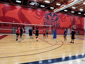 Either people stand around a volleyball court listening to an instructor.