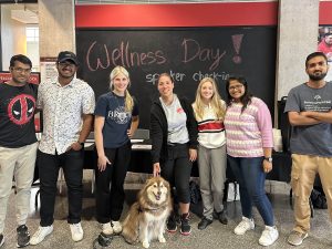 Seven people stand together in front of a large chalkboard that reads 