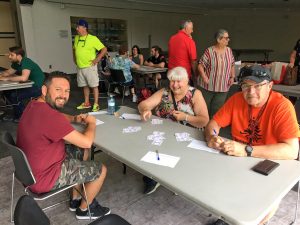 Three people sit at a table with playing cards in piles.