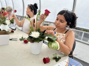 Four people sit at a table, each arranging flowers into a vase.