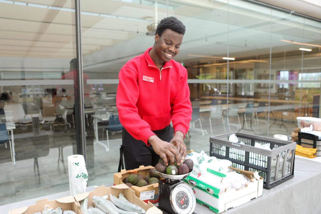 A young man in a red shirt arranges avocadoes on a scale.