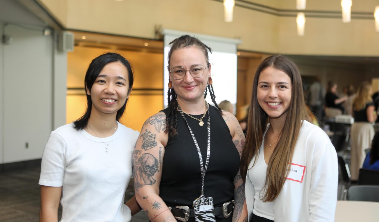 Three women pose for a photo in a sunny meeting room.