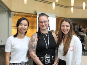 Three women pose for a photo in a sunny meeting room.