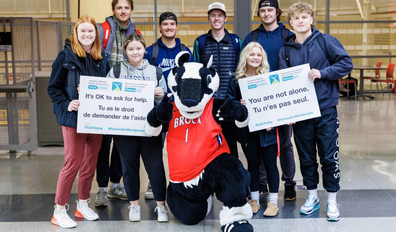 A group of Brock student-athletes pose with the University’s mascot, Boomer the Badger. Two students hold signs that read “It’s OK to ask for help” and “You are not alone.”